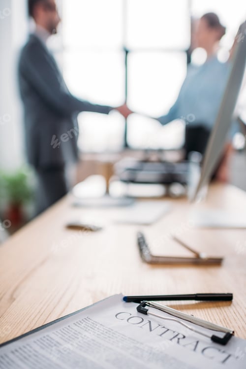 Preview: close-up shot of business contract lying on table and blurred business partners shaking hands on