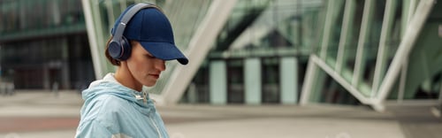 Preview: Sportive woman in headphones stands with bottle of water after running in city. Healthy lifestyle
