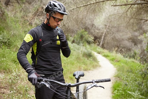 Preview: Outdoor portrait of handsome professional rider in cycling clothing holding handlebar of black motor