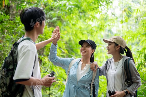 Preview: Backpacker tourist man woman friend group high five clapping hand while hiking or trekking in forest