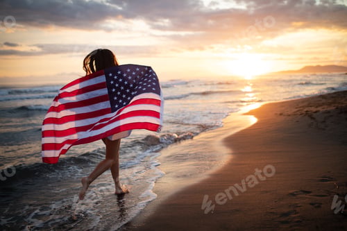 Preview: Cheerful happy woman outdoors on the beach holding USA flag having fun