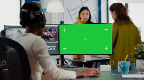 Preview: Black videographer with headphones using computer with green screen