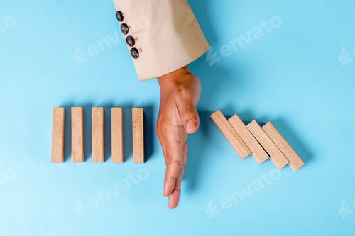 Preview: Businessman's Hand Stopping Falling Dominoes, Symbolizing Intervention And Control