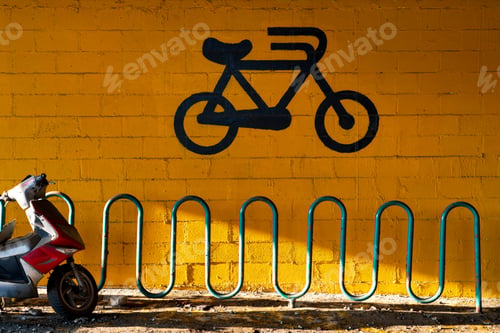 Preview: Bright yellow urban wall with black bicycle graffiti and teal metal bike rack,
