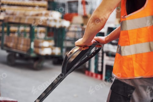 Preview: Young male worker in uniform is in the warehouse pushing pallet truck