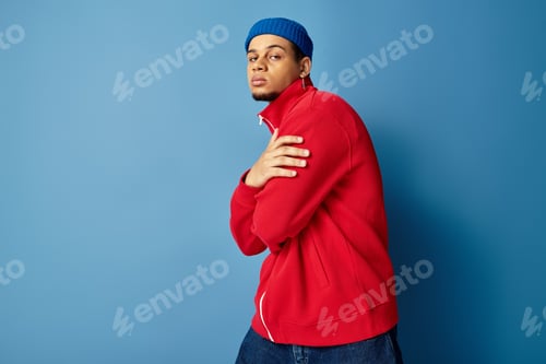 Preview: Stylish young african american man wearing beanie and red jacket against blue backdrop
