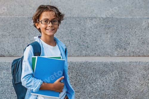 Preview: Portrait of happy caucasian young school boy with backpack holding notebook outside