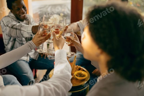 Preview: Close up of happy friends is drinking cocktails and clinking glasses during dinner party at