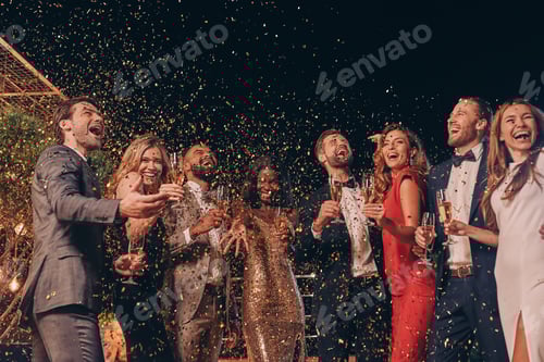 Preview: Group of happy people in formalwear having fun together with confetti flying all around