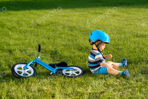 Preview: Boy in helmet sitting on grass with blue balance bike