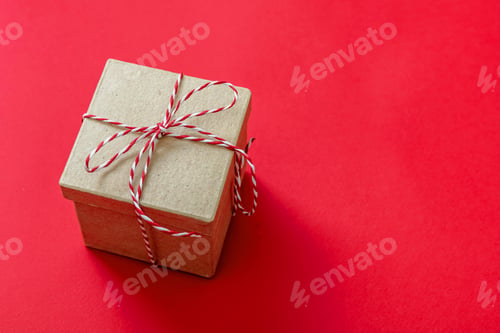 Preview: Christmas gift box on red color background. Red white striped string tied on brown kraft present.