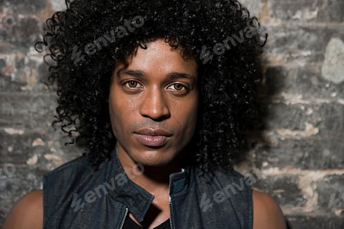 Preview: Portrait of a person with curly hair against a brick wall backdrop.