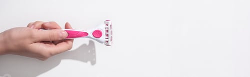 Preview: cropped view of woman holding female pink razor on white background, panoramic shot