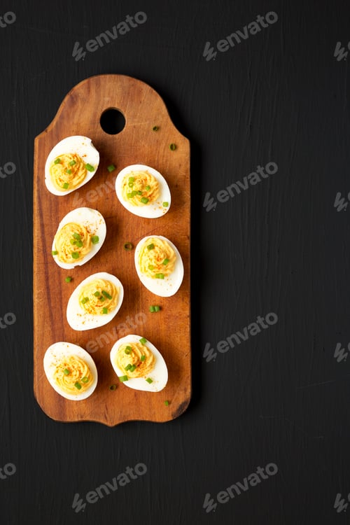 Preview: Homemade Deviled Eggs with Chives on a rustic wooden board on a black surface, top view.