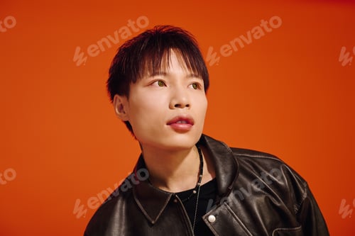 Preview: Stylish asian man posing confidently against a vibrant orange backdrop during sunset