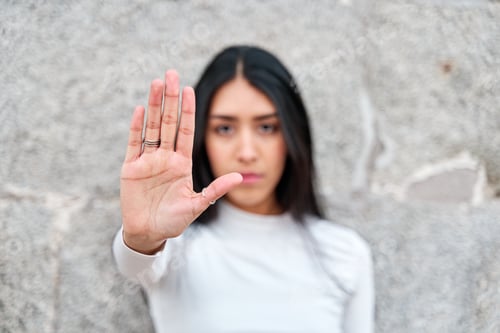 Preview: Young woman out of focus showing concerned palm of hand in focus.
