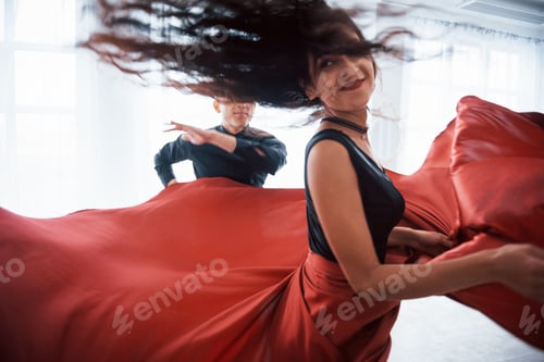 Preview: Photo of motion. Young pretty woman in red and black clothes dancing with bald guy in the white room