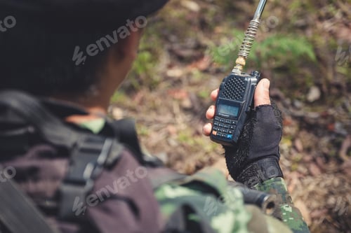 Preview: Closeup image of an armed soldier holding and using radio communication in the battle field