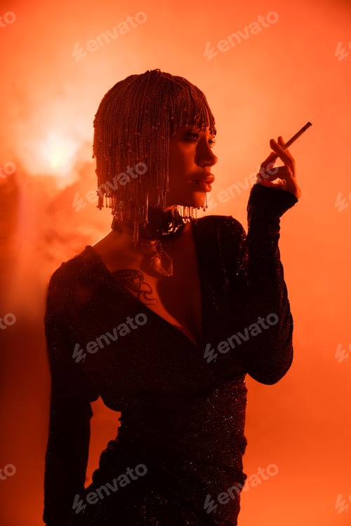 Preview: sexy woman in metallic headwear and black dress standing with cigarette on orange background with