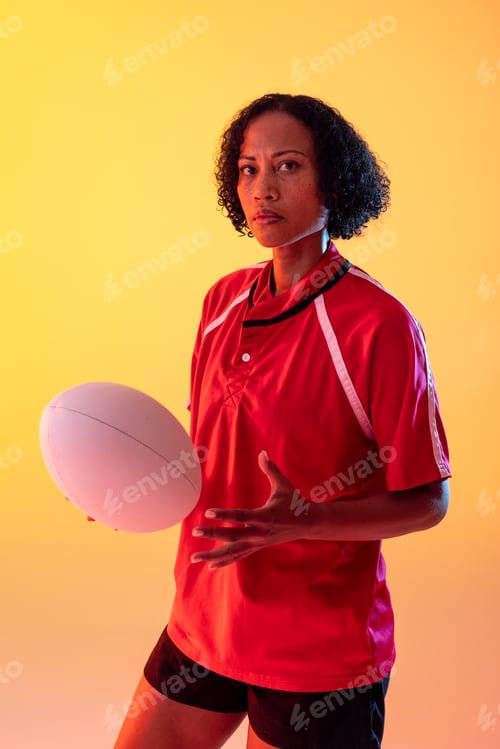Preview: Portrait of african american female rugby player with rugby ball over neon yellow lighting