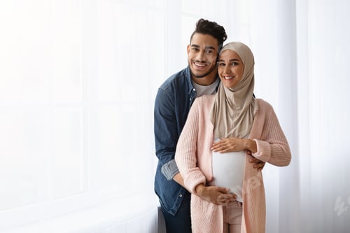 Preview: Pregnant Muslim Woman And Her Husband Embracing Near Window At Home