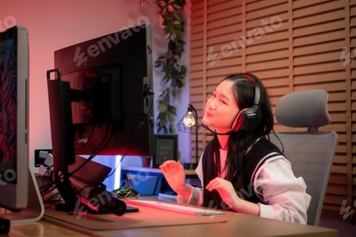 Preview: Teenage girl gamer wearing headphones and playing on a desktop computer in a colorful gaming setup