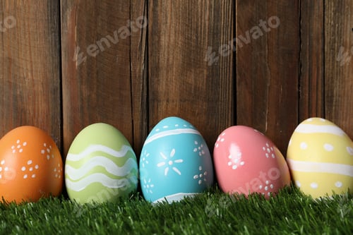 Preview: Colorful painted Easter eggs on green grass against wooden background, space for text