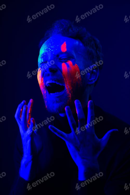 Preview: Fashion portrait. A man with fluorescent paint on his face under neon light.