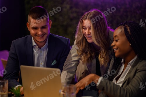 Preview: Cheerful work colleagues working on a laptop while having a meeting in a cafe
