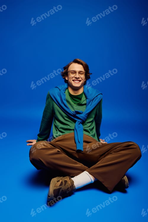 Preview: Young man showcasing modern fashion with confidence in a vibrant blue setting