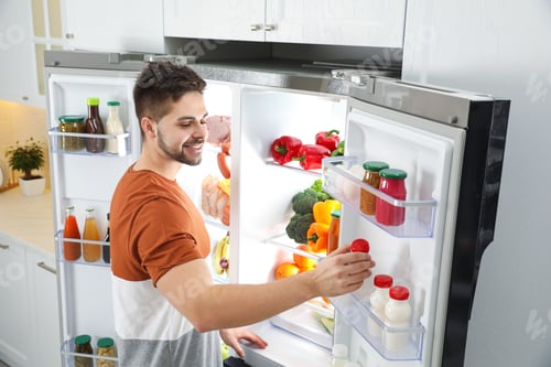 Preview: Young man taking yoghurt out of refrigerator indoors