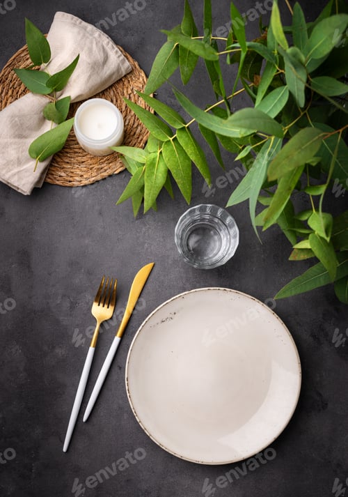 Preview: Table setting with a empty beige plate, a glass, a candle and a napkin with eucalyptus branches