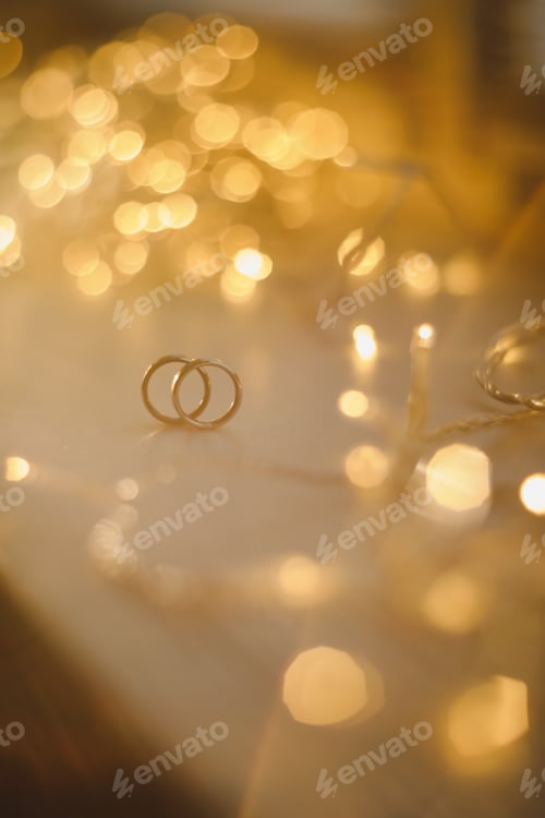 Preview: Wedding rings on blured bokeh glowing golden background. Symbol of love and romance on a textured