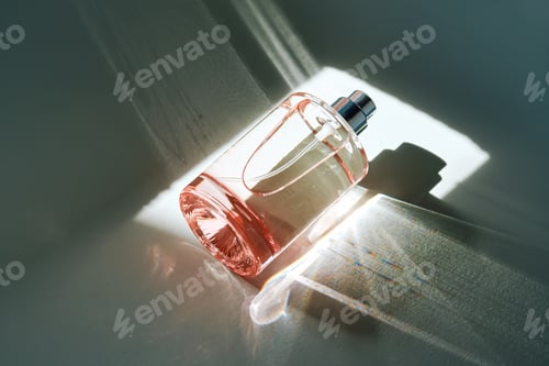 Preview: Pink perfume bottle on the light background in the rays of sun with highlights.