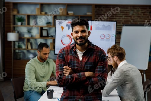 Preview: Confident smiling Indian guy, startup team leader, standing in front of mixed race office workers or