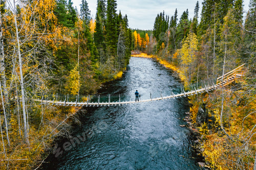 Preview: Aerial view of autumn fall leaf color in the woods blue river with suspension bridge with traveler