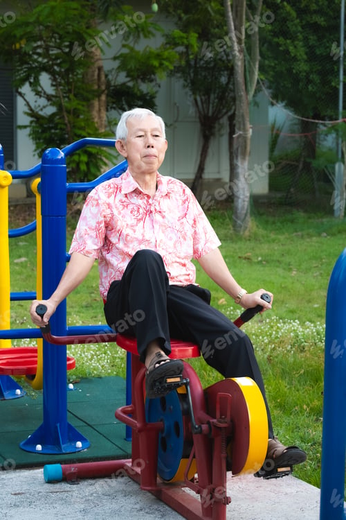 Preview: Candid shot of focused senior Asian man working out outdoor exercise equipment.
