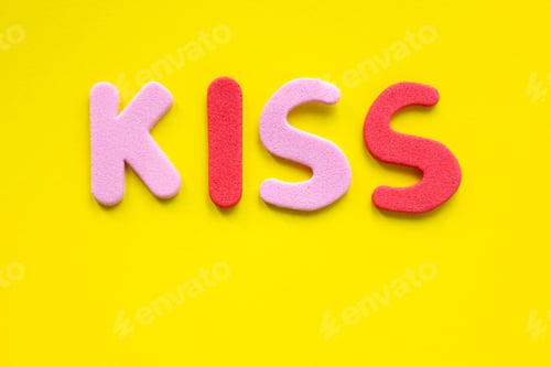 Preview: The word Kiss from red and pink letters of the alphabet on a yellow background with copy space.