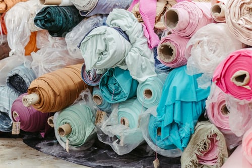 Preview: Vibrant collection of multicolored fabric rolls and swatches, arranged in a neat pile