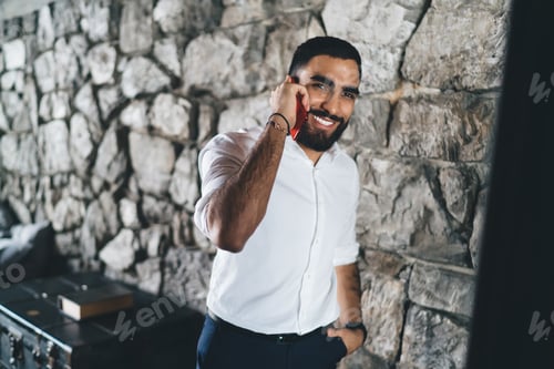 Preview: Positive man standing near stone wall having phone call