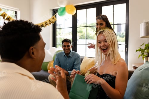 Visualização: Comemorando aniversário, mulher alegre com amigos abrindo presente em festa em casa