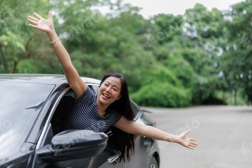 Preview: Happy woman enjoying road trip leaning out of car window