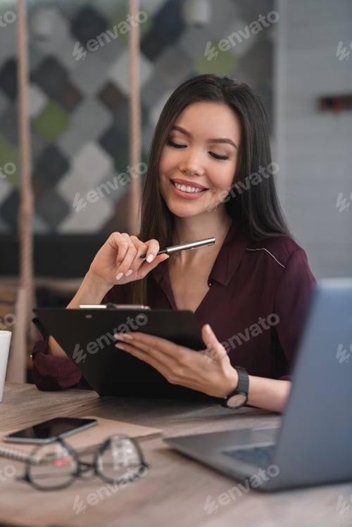 Preview: Smiling Woman Holding Pen and Clipboard at Desk