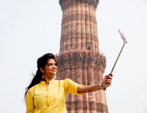 Preview: Tourist woman taking selfie in front of Qutub Minar, Delhi, India.