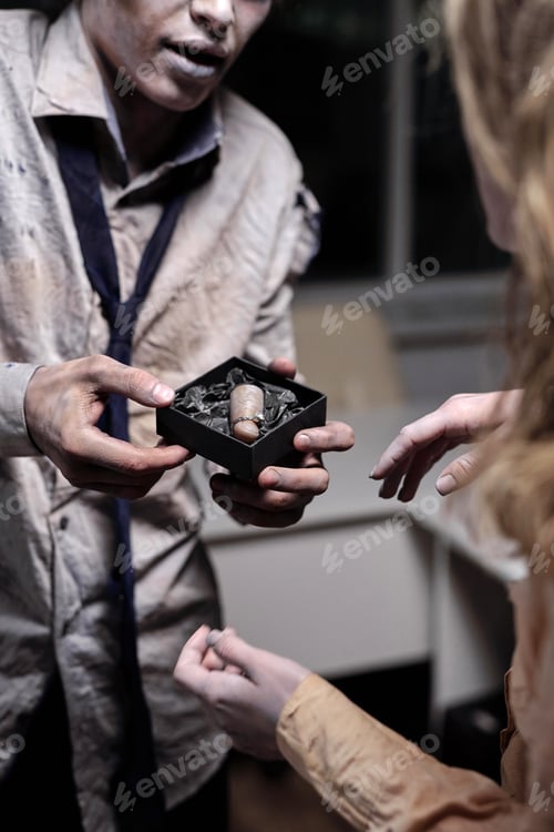 Preview: Hands of dead businessman showing small box containing cut finger with diamond ring to zombie female