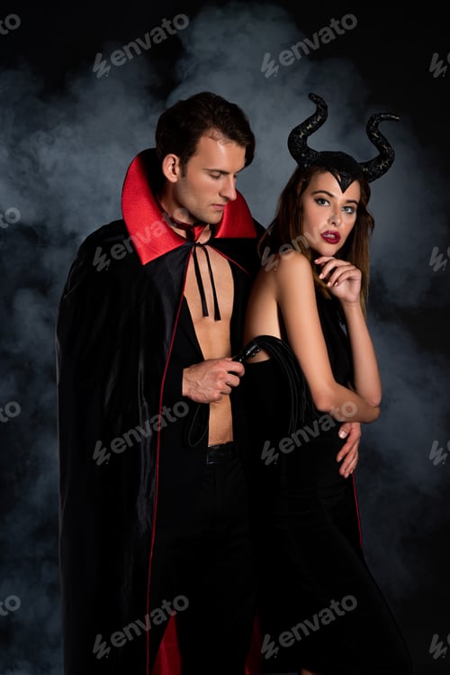 Preview: handsome man in cloak holding flogging whip near woman with horns on black with smoke