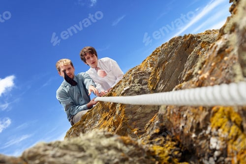 Preview: Businessmen pulling rope over cliff