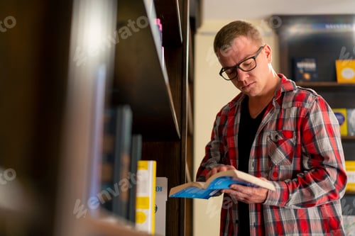 Preview: guy in glasses stands near the bookshelves reads a book enthusiastically at story in the library
