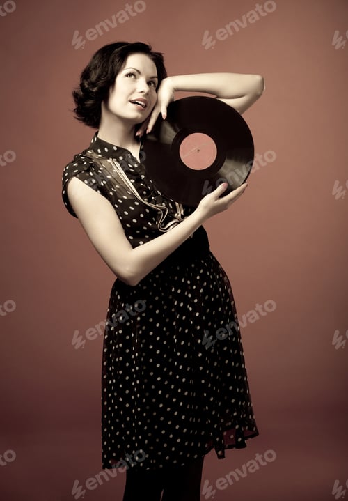 Preview: Young woman in vintage dress standing and holding vinyl record in hands