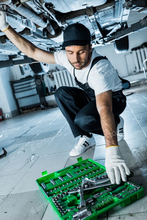 Preview: selective focus of car mechanic taking metallic tool from toolbox while repairing automobile